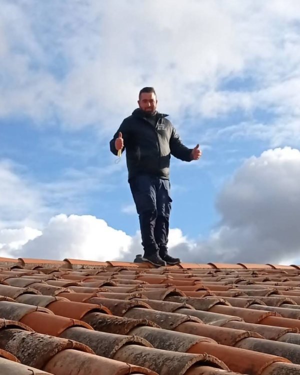 Yves Marchal debout sur un toit en tuiles canal, pouce levé.